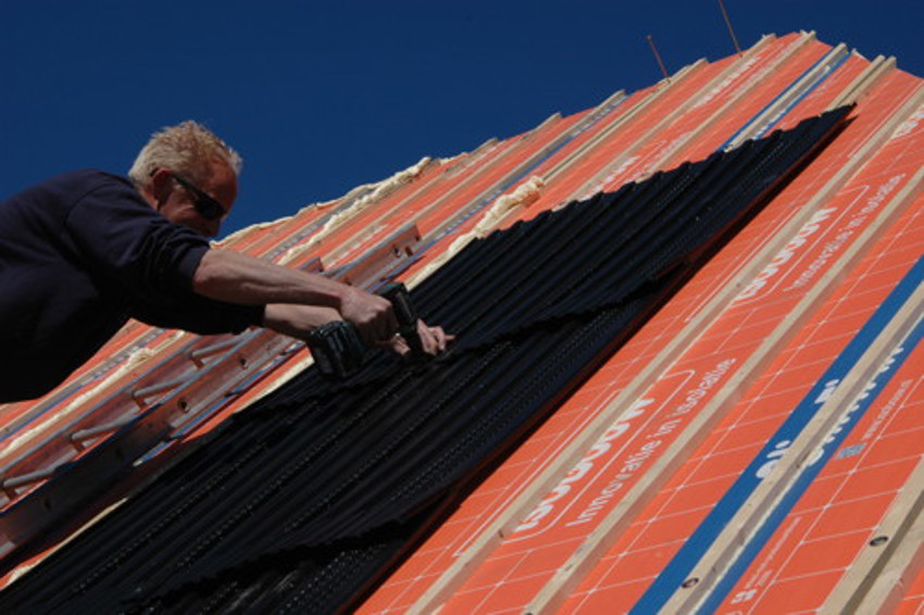 Close-up van oranje dakelementen en een dakdekker die een solar module hierop aan het bevestigen is. 