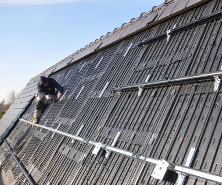 Projectfoto van een dakdekker die een solar paneel bevestigd op het hellende dak. 