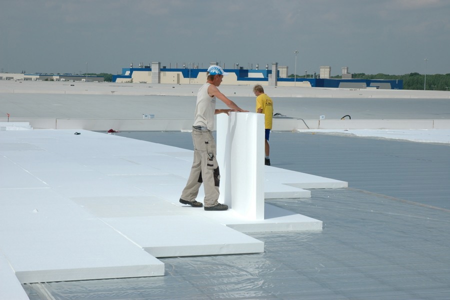 Projectfoto van een plat dak waar mannen witte EPS isolatieplaten van BEWI IsoBouw leggen. 